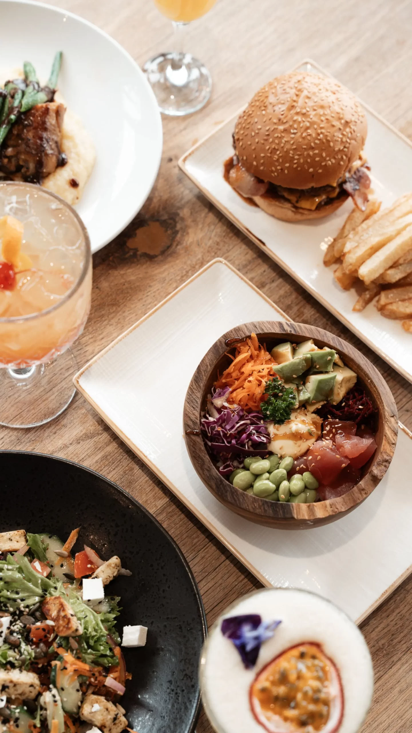 Table spread with gourmet burger, poke bowl, and cocktails at The Beach Bar Hout Bay.